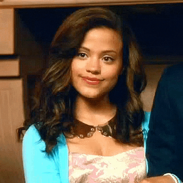 a woman is wearing a blue cardigan and a pink dress and smiling .