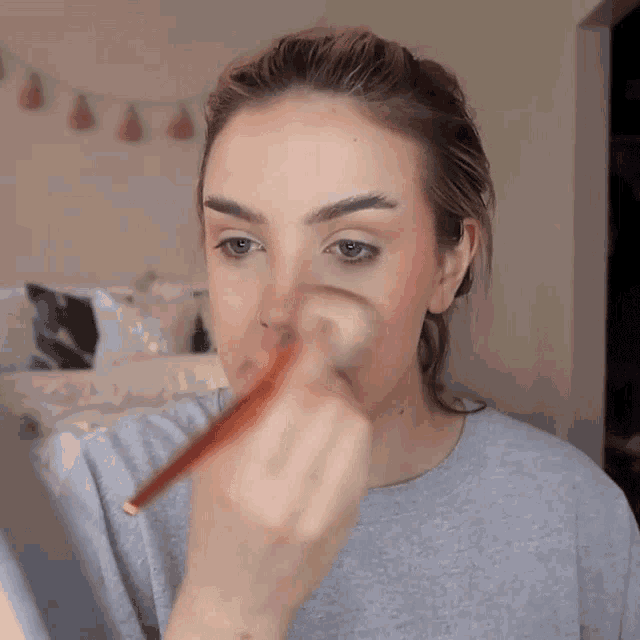 a woman is applying makeup with a brush to her face