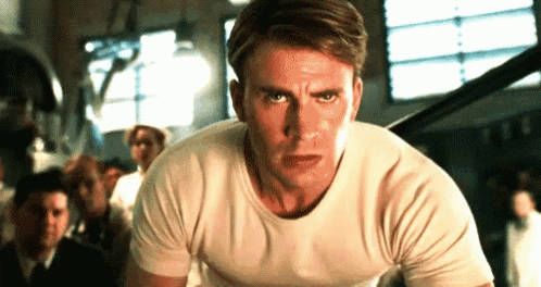 a man in a white t-shirt is standing in a gym with a group of people behind him .