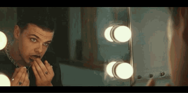 a man is applying lipstick in front of a mirror with lights .