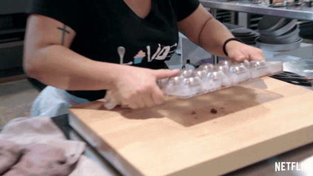 a woman wearing a black shirt that says love is cutting eggs on a wooden cutting board
