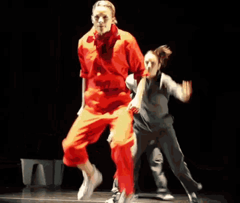 a group of people are dancing on a stage and one of them is wearing red