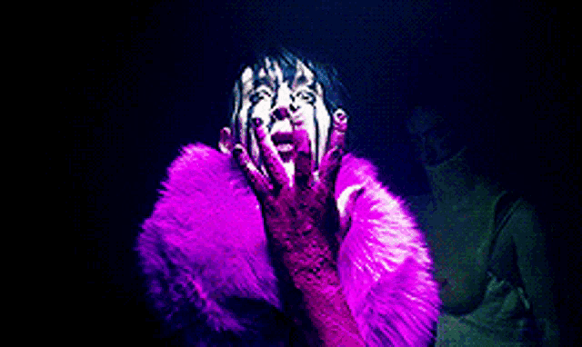 a woman wearing a purple fur coat and pink gloves is covering her mouth with her hands .