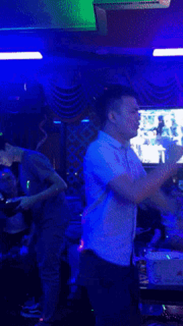 a man in a white shirt is holding a microphone in front of a television