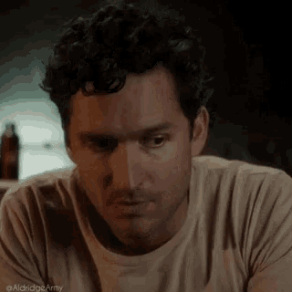 a man with curly hair is sitting at a table with his eyes closed and a serious look on his face .
