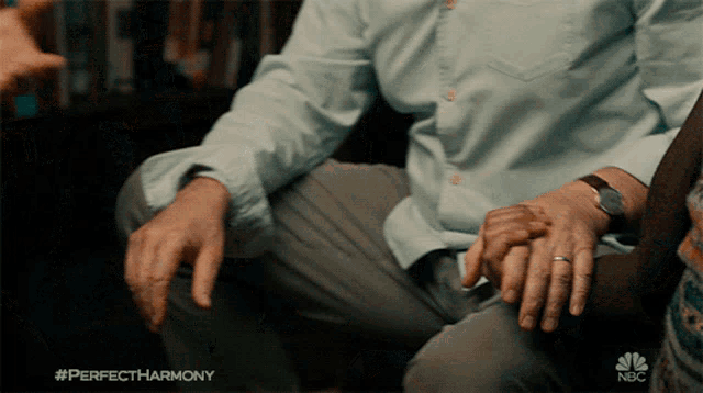 a man holding another man 's hand with a nbc logo behind him