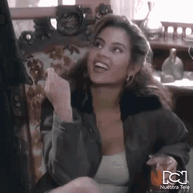 a woman in a leather jacket is sitting on a couch holding a glass of wine and giving the middle finger .
