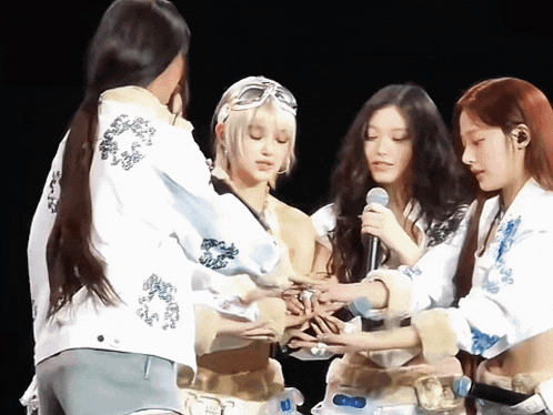 a group of young women gathered around a microphone with a bottle of water in the foreground