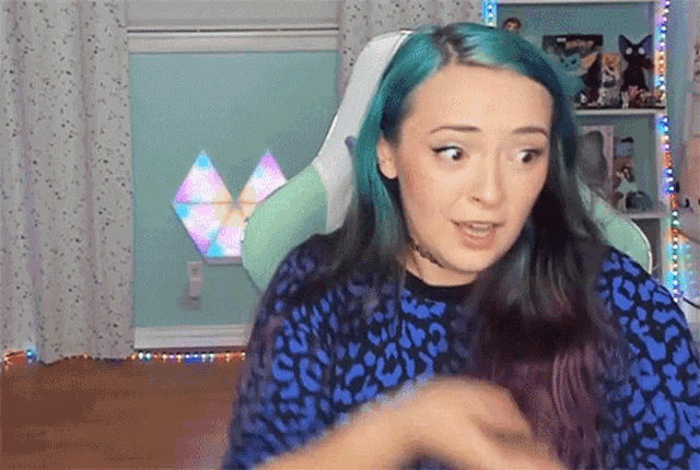 a woman with blue hair is sitting in a chair and making a funny face