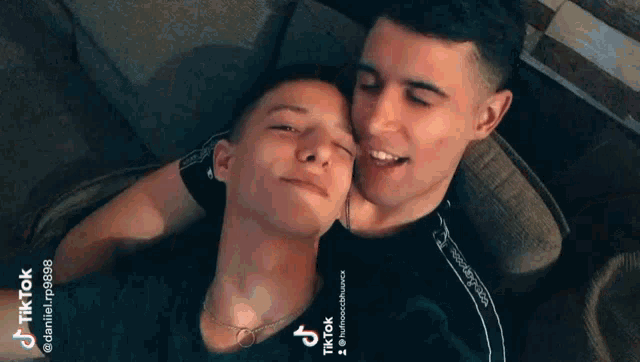 two young men are laying on a couch with their heads together .