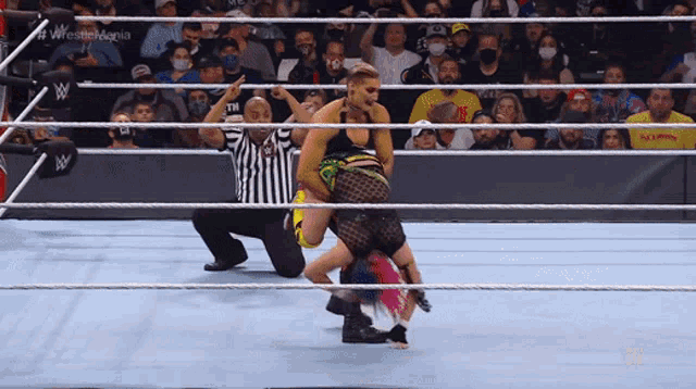 a wrestler is being lifted in the air by another wrestler while a referee watches on