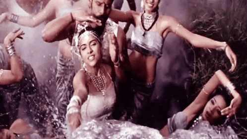 a group of women are dancing in the water and one of them is wearing a necklace that says ' a ' on it