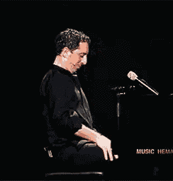 a man is singing into a microphone in front of a piano that says music