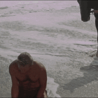 a shirtless man is kneeling on the beach near the ocean