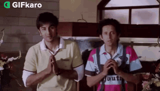 two men are standing next to each other with their hands folded in front of a window with a gifkaro logo in the corner