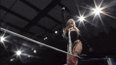 a wrestling match is going on in a dark room with lights shining through the ropes
