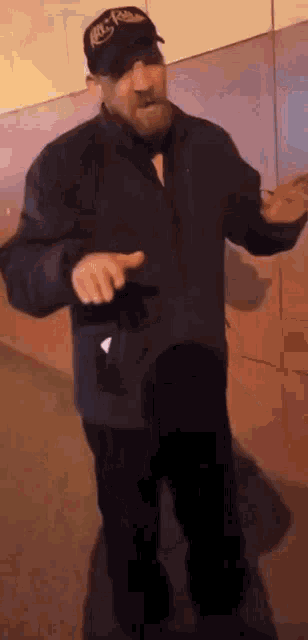 a man with a beard wearing a hat and a jacket is standing in front of a wall .