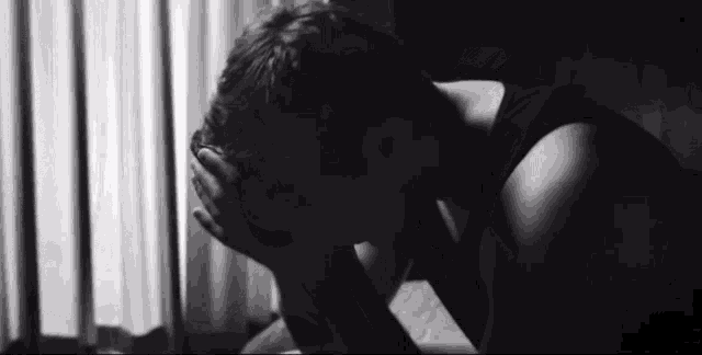 a black and white photo of a man covering his face with his hands .