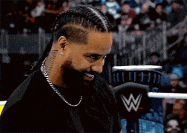 a man with braids and a beard is standing in a wrestling ring and smiling .