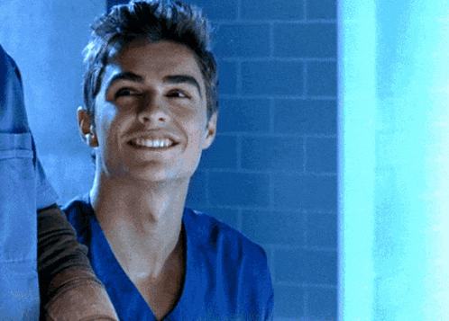 a man in a blue scrub top smiles in front of a blue wall
