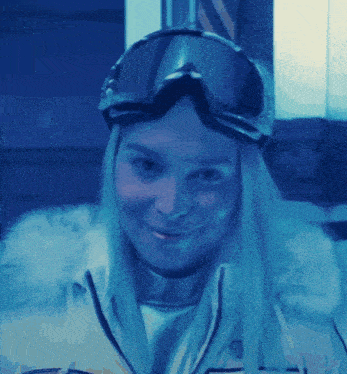 a woman wearing ski goggles is smiling in a blue light