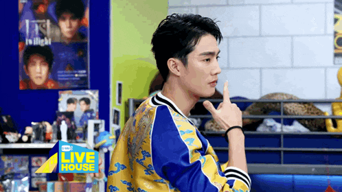 a man in a blue and yellow jacket is making a funny face while holding his finger to his mouth .