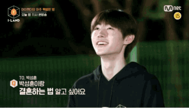 a young man in a black hoodie is smiling with a mnet logo behind him