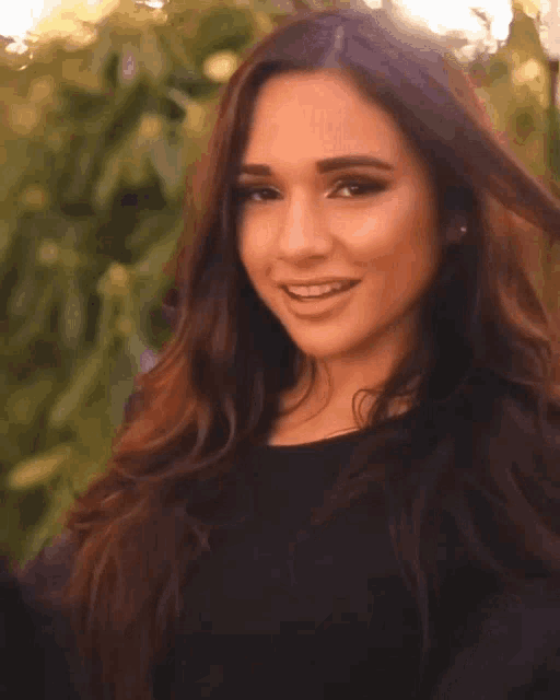 a woman with long brown hair is smiling and wearing a black top