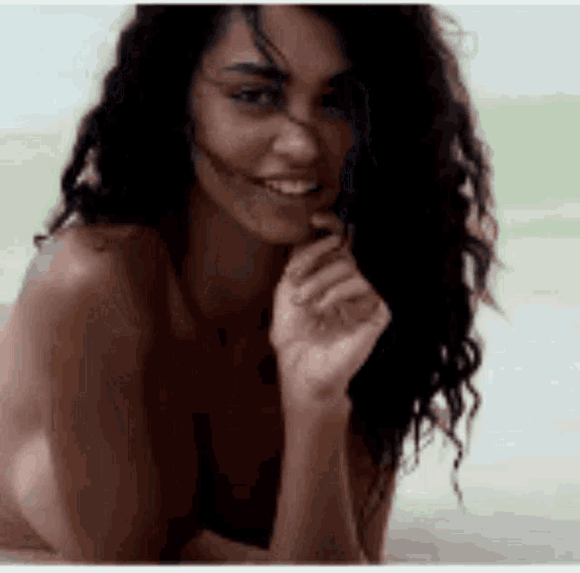 a naked woman with long curly hair is smiling and looking at the camera .