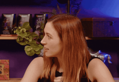 a woman is sitting in front of a shelf with magic cards on it
