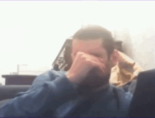 a man in a blue shirt is covering his face with his hand .