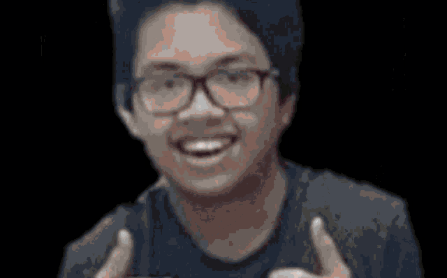 a young man wearing glasses is smiling and holding a cell phone in his hand .