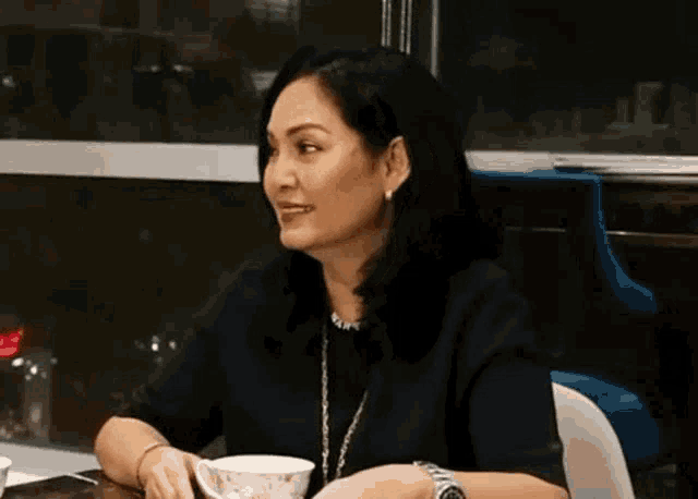 a woman in a black shirt is sitting at a table with a cup of tea .