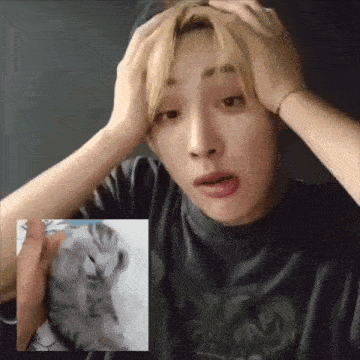 a man is holding his head in his hands while looking at a picture of a cat .