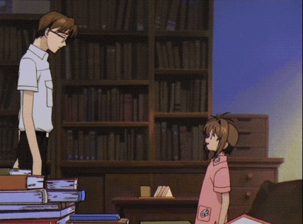a man wearing glasses and a white shirt smiles in front of a bookshelf