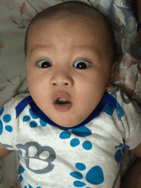 a baby wearing a blue and white paw print shirt makes a funny face