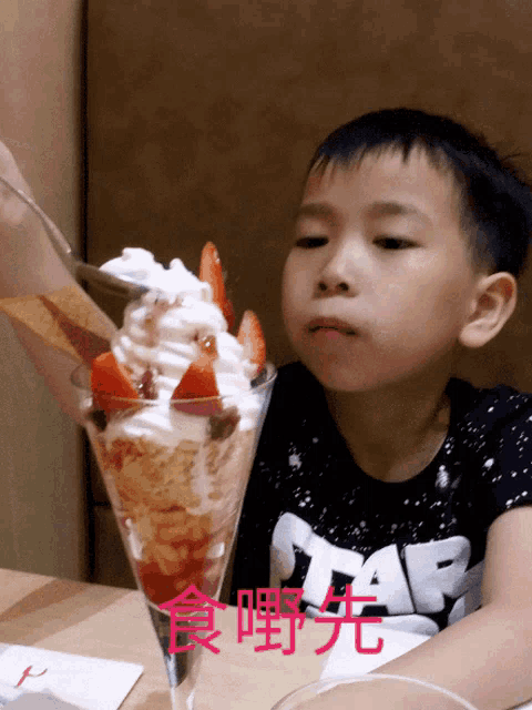 a young boy wearing a star wars shirt is eating a ice cream sundae