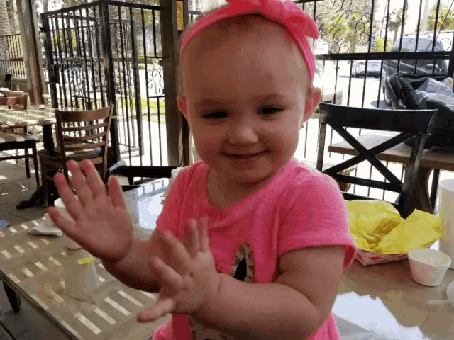 a little girl wearing a pink shirt and a headband is clapping her hands