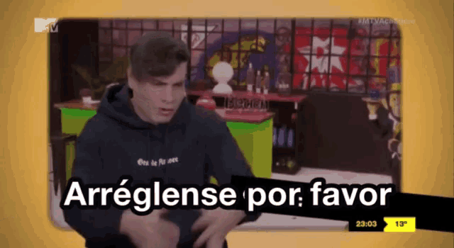 a man in a black hoodie stands in front of a tv screen that says " arreglense por favor "