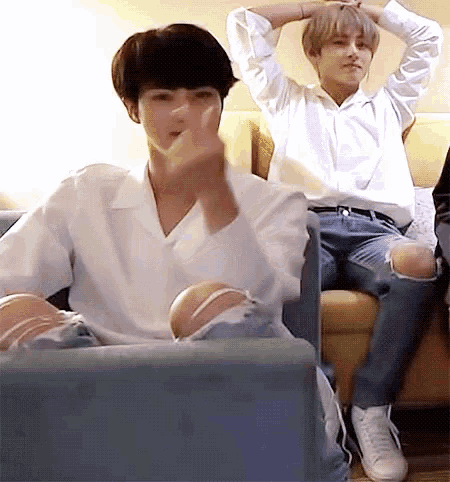 a man in a white shirt is sitting on a couch next to another man in jeans .
