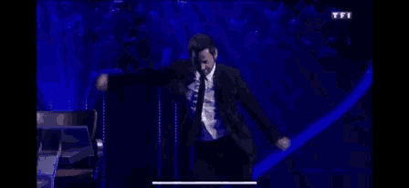 a man in a suit and tie is dancing on a blue stage .