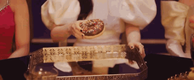 a woman in a white dress is holding a donut with sprinkles on it