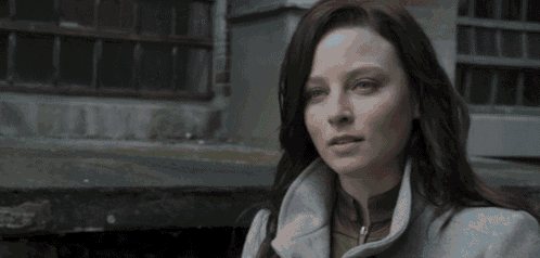 a woman wearing a grey coat looks at the camera