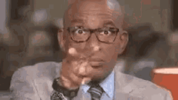 a bald man in a suit and tie is pointing at the camera .