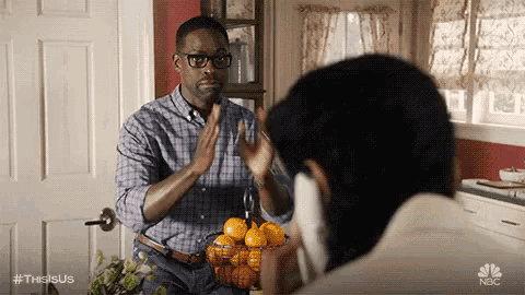 a man is holding a basket of oranges and talking on a cell phone while another man looks on .