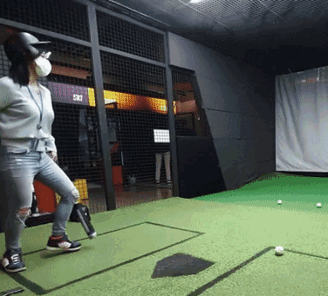 a woman wearing a mask and a baseball helmet stands on a green field