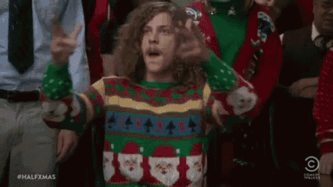 a man wearing an ugly christmas sweater is standing in front of a crowd .