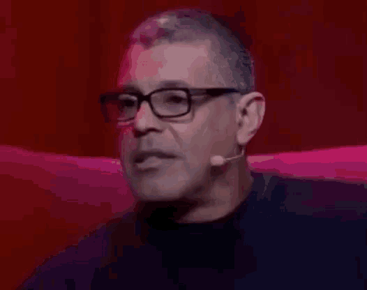 a man wearing glasses and a microphone is sitting on a red chair .
