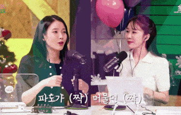 two women are sitting in front of a microphone with balloons in the background and one of them is wearing headphones