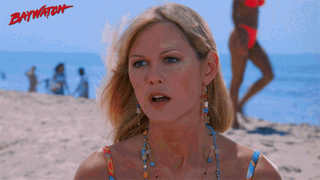 a woman stands on a beach with the word baywatch on the bottom